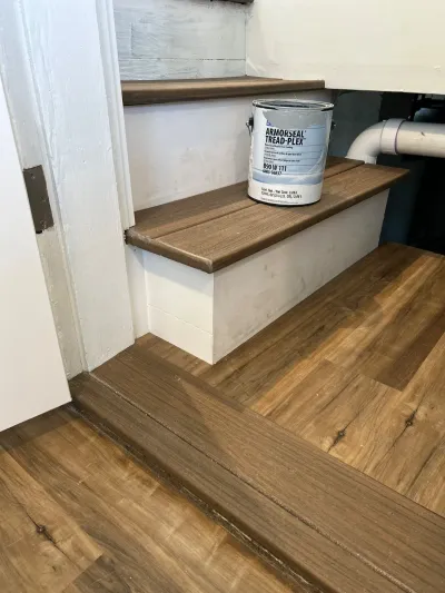 Basement stairs with painted white risers, stained treads, and a can of floor coating on one step.