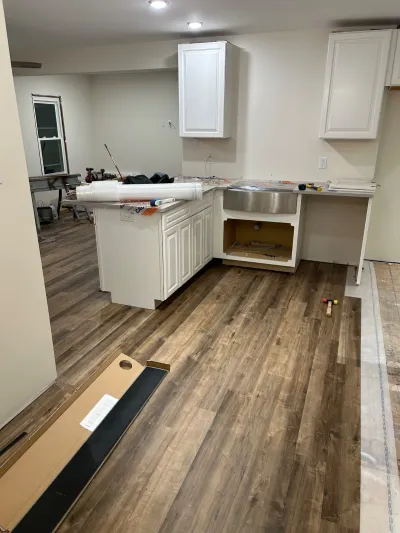 Kitchen mid-renovation with white cabinets, new plank flooring, and a sink installed before countertops.