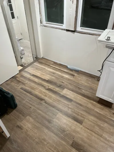 A kitchen mid-renovation with new wood-look vinyl plank flooring installed and unfinished drywall walls.