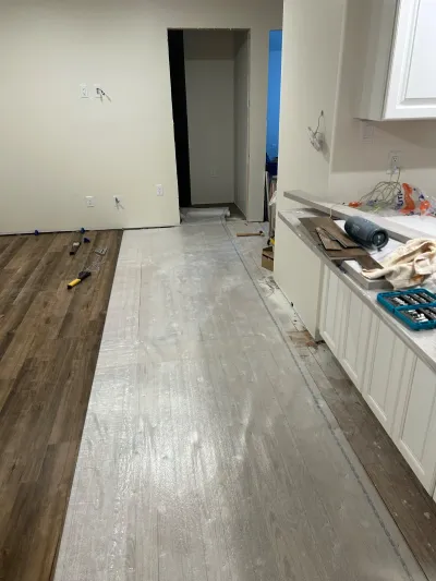 Kitchen mid-renovation showing new grey plank flooring being installed next to older dark wood flooring.
