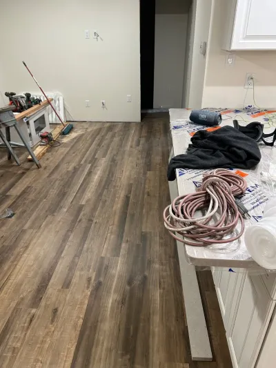 Kitchen mid-renovation with new wood-look flooring, tools, and a plastic-covered countertop.