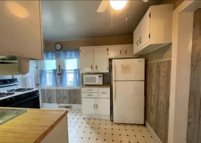 Dated kitchen with white cabinets, wood paneling, vinyl flooring, and an aging white refrigerator.