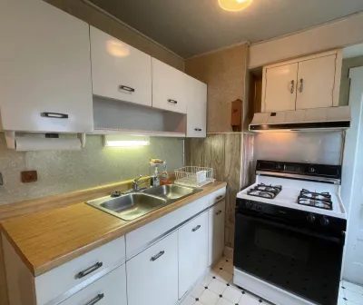 A dated kitchen with white laminate cabinets, wood paneling, and a vintage white gas range.
