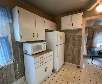 Dated kitchen with white cabinets, wood paneling, and a refrigerator before renovation.