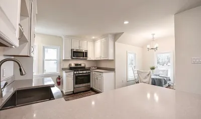 Bright white kitchen with quartz counters, stainless appliances, and an open view into a sunlit dining nook.