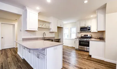 Bright white kitchen with a peninsula, stainless appliances, and dark wood-look flooring.
