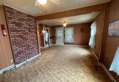 Dated living room with wood paneling, brick accent wall, worn carpet, and an open archway to another room.