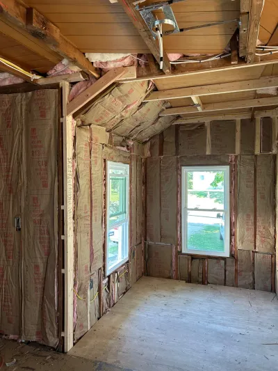 Room under construction with exposed insulation, wood framing, and rough electrical wiring.