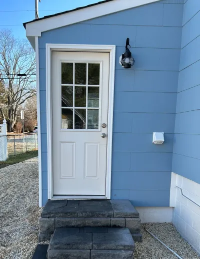 Blue-sided building exterior with a white paneled door, lantern light, and stone paver steps.