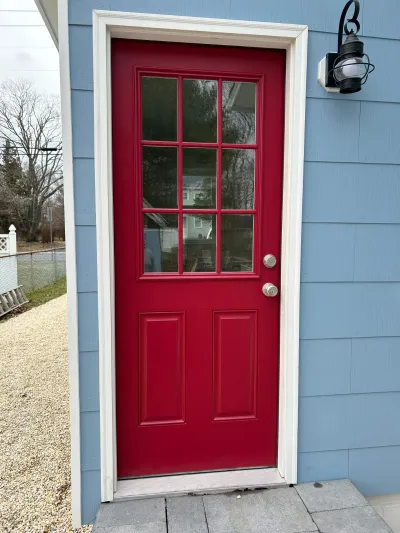 A red paneled entry door with nine glass panes set into blue-grey siding, beside a black lantern light.