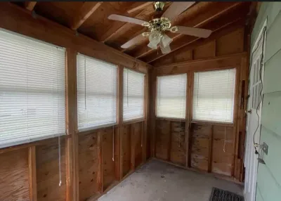 An unfinished sunroom with exposed wood framing, plywood walls, and a vaulted ceiling with a fan.