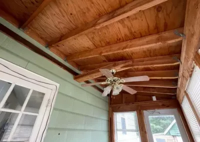 Porch ceiling under renovation with exposed wood rafters and an installed ceiling fan.