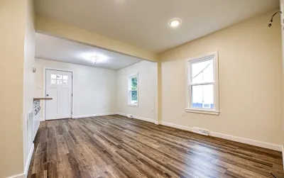 Empty renovated living room and entryway with wood-look vinyl plank flooring and white trim.