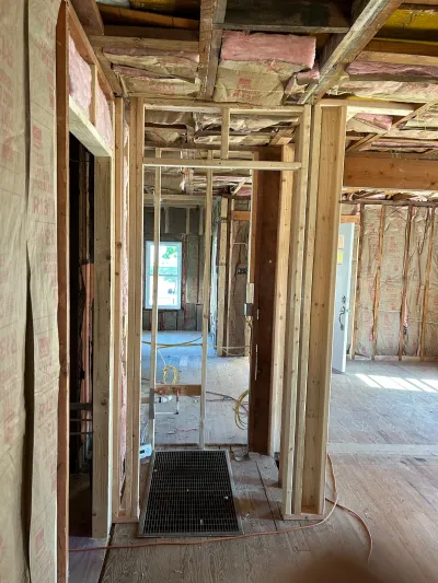 Interior of a home mid-renovation showing exposed wood framing, insulation, and rough-in electrical wiring.
