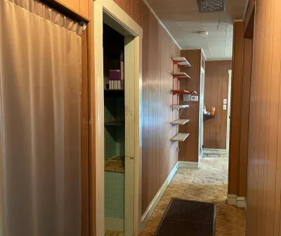 A dated hallway with wood paneling, a drop ceiling, worn carpet, and a curtain-covered doorway.