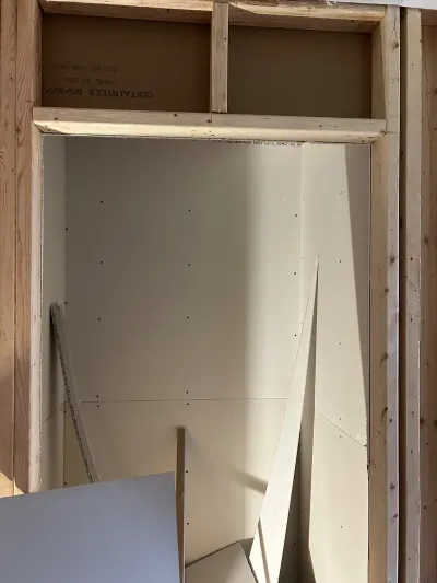 Framed closet opening with drywall hung but not yet taped or finished, cut panels leaning nearby.