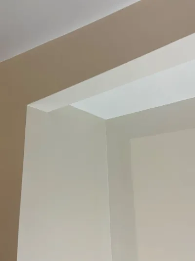 Close-up of a painted doorway corner where a tan wall meets white trim and ceiling.