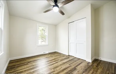 Empty bedroom with vaulted ceiling, dark wood-look flooring, ceiling fan, and white bifold closet doors.
