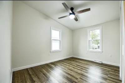Empty bedroom with vaulted ceiling, wood-look flooring, a ceiling fan, and two windows.