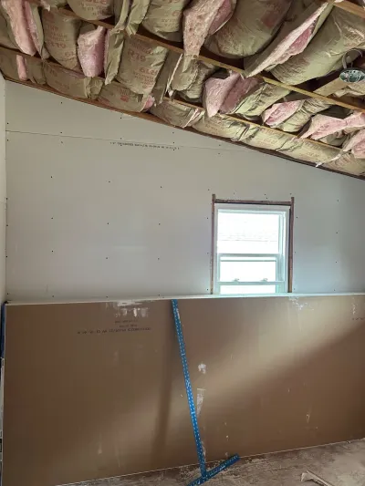 Room under construction with exposed insulation in a vaulted ceiling and drywall panels not yet installed.