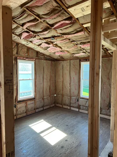Unfinished room mid-construction with exposed studs, insulation, and framed vaulted ceiling.