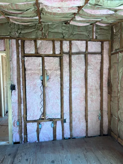 Unfinished room with exposed wall studs, pink batt insulation, and rough electrical wiring during construction.