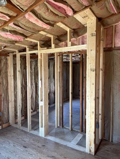 Unfinished interior framing with exposed studs, insulation overhead, and a rough door opening leading to another room.