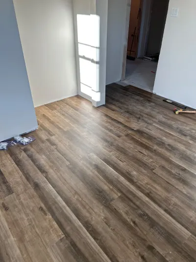 Newly installed dark wood-look vinyl plank flooring in a room with unfinished baseboards and tools left on the floor.