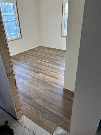 A room under renovation with new plank flooring installed and an untrimmed doorway leading to it.