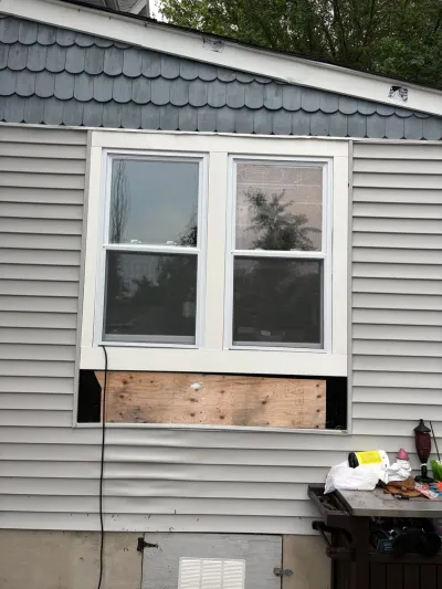 Exterior wall mid-repair showing two windows, patterned shingle siding above, and a plywood patch below.