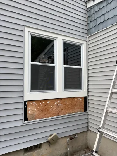 Exterior wall mid-repair with new window trim installed and a plywood patch below awaiting siding.