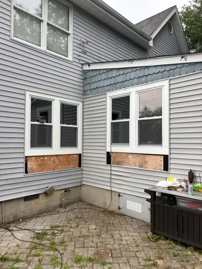 Exterior corner of a house with plywood patched below two windows during a siding or window renovation.