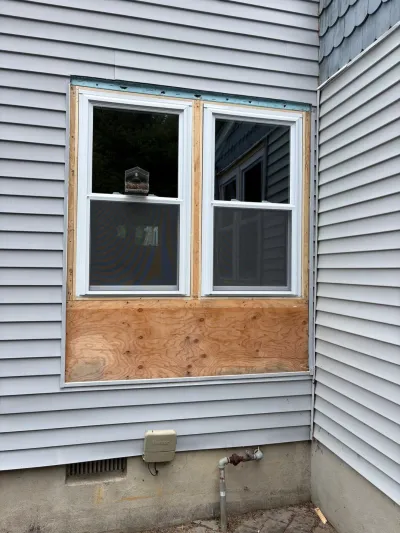 Exterior wall mid-renovation showing new vinyl siding around windows with bare plywood still exposed below.