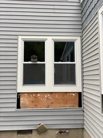 Exterior wall with two windows and an unfinished plywood patch below awaiting new siding.