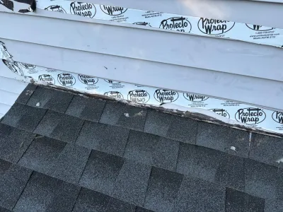 Close-up of roof-to-wall flashing membrane installed beneath vinyl siding above asphalt shingles.