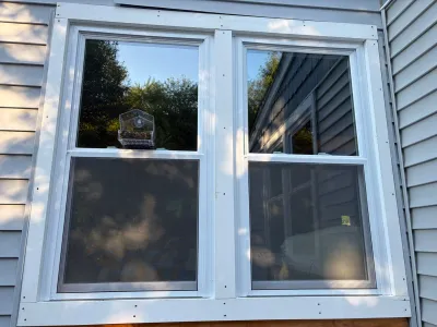 Two white vinyl double-hung windows on a house exterior with a bird feeder mounted between them.