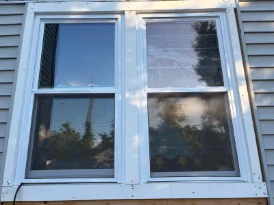 Two new white vinyl double-hung windows installed in grey siding, with one pane showing a hazy film.