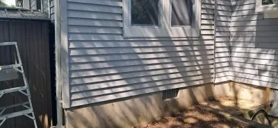 Exterior corner of a house with new grey vinyl siding installed above an exposed concrete foundation.