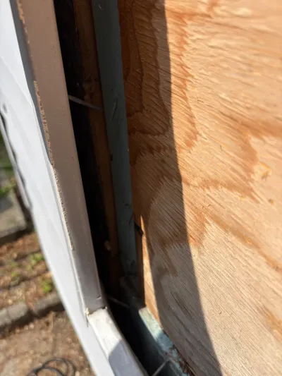 Close-up of exposed wood sheathing with water staining beside newly installed white siding.