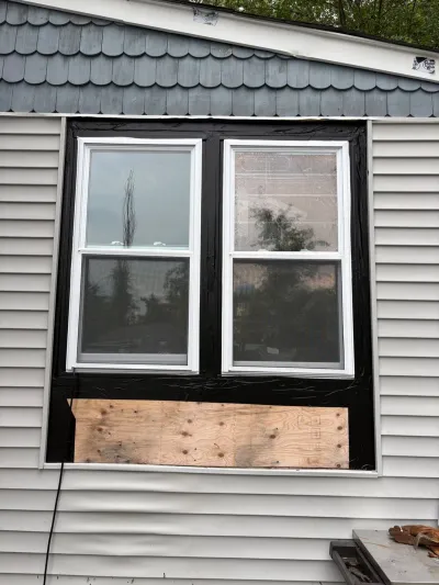 New double-hung windows installed with black flashing tape and an exposed plywood patch below awaiting siding.