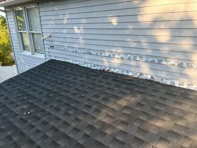 Close-up of a roof-to-wall flashing membrane installed where vinyl siding has been removed above shingles.