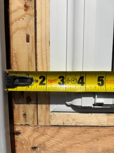 Close-up of a tape measure spanning a rough window opening framed with wood studs during construction.