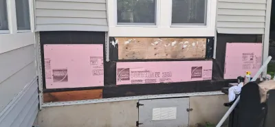 Exterior wall under repair with vinyl siding removed and pink foam insulation boards installed beneath windows.
