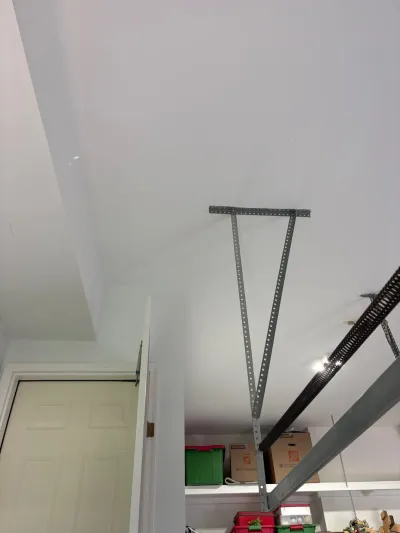 Garage ceiling with a metal overhead storage rack bracket above shelves holding bins and boxes.