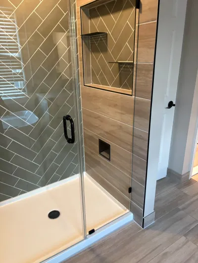 Walk-in glass shower with herringbone tile walls, black hardware, and a built-in storage niche.