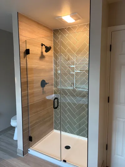 A walk-in shower with wood-look tile walls, herringbone tile accent, glass door, and matte black fixtures.