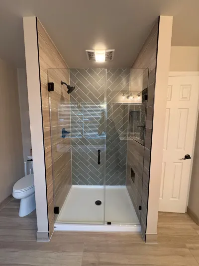 A finished walk-in shower with herringbone tile, wood-look tile walls, glass doors, and matte black hardware.