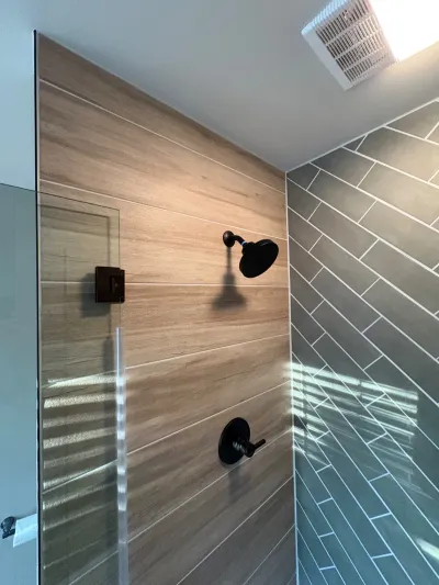 Walk-in shower with wood-look tile on one wall and diagonal gray tile on the other, finished with matte black fixtures.