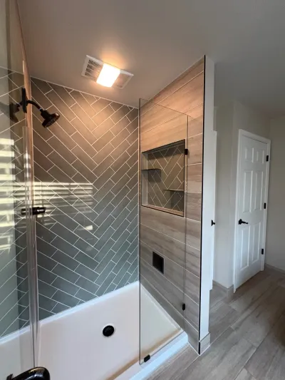 Bathroom with herringbone tile tub surround and wood-look tile shower behind frameless glass.