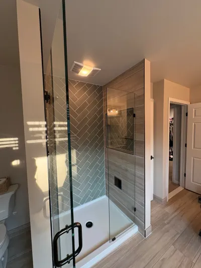 A walk-in shower with herringbone tile and wood-look tile walls, framed by a frameless glass door with black hardware.